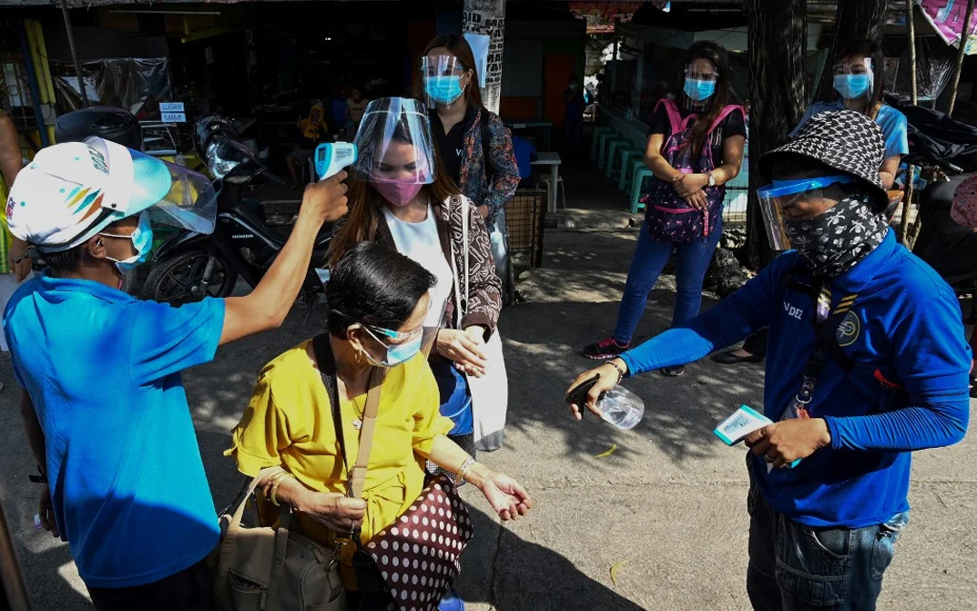 Passengers wearing face shields as their temperatures are taken before boarding a bus in Manila