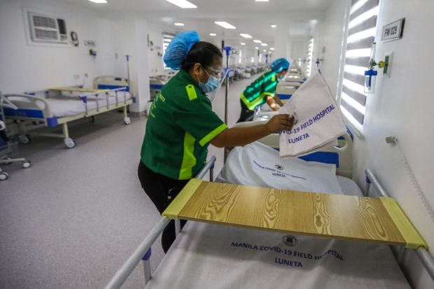 Workers clean beds inside a ward of a field hospital for Covid-19 coronavirus patients at a park in the Manila on June 24, 2021. - (Photo by Maria TAN / AFP)