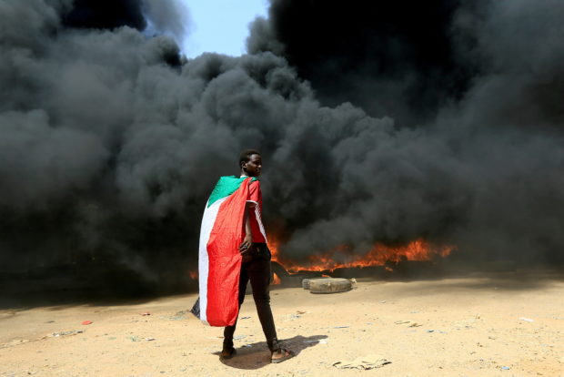 FILE PHOTO: A person wearing a Sudan's flag stand in front of a burning pile of tyres during a protest  against prospect of military rule in Khartoum, Sudan October 21, 2021. REUTERS/Mohamed Nureldin Abdallah//File Photo