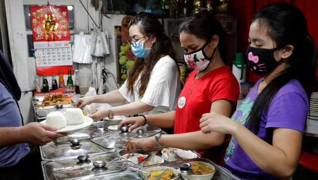 Women wearing protective masks serve food at a small restaurant in Manila, Philippines