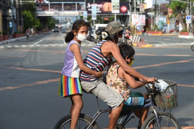FILE PHOTO: A father with his children aboard their bicycle crosses an almost empty road in Manila on March 20, 2020, after the government imposed an enhanced community quarantine against the rising numbers of coronavirus infections. AFP