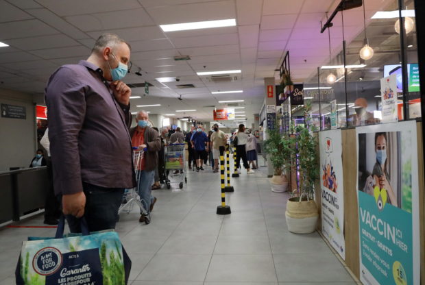 FILE PHOTO: A shopper, wearing a protective face masks, looks at a poster for a coronavirus disease (COVID-19) vaccination centre installed inside a supermarket in Brussels, Belgium, August 30, 2021. REUTERS/Bart Biesemans