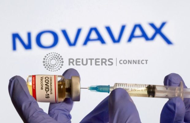 FILE PHOTO:  A woman holds a small bottle labeled with a "Coronavirus COVID-19 Vaccine" sticker and a medical syringe in front of displayed Novavax logo in this illustration taken, October 30, 2020. REUTERS/Dado Ruvic/File Photo/File Photo
