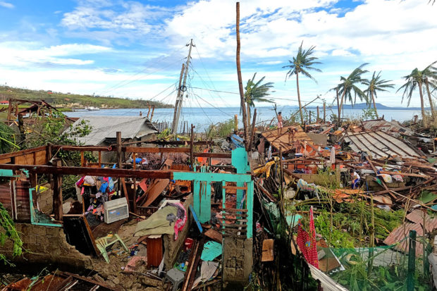 This photo taken on December 17, 2021 shows residents standing by their houses destroyed by Super Typhoon Rai after the storm crossed over Surigao City in Surigao del Norte province. (Photo by Erwin MASCARINAS / AFP)