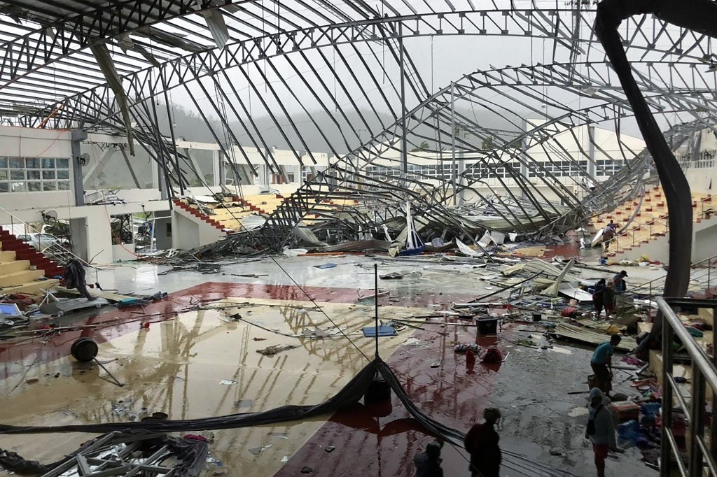 odette In this photo taken on December 16, 2021, people stand inside a sport complex building whose roof collapsed at the height of Super Typhoon Rai in Dapa town, siargao Island, Surigao del norte province. (Photo by Roel CATOTO / AFP)