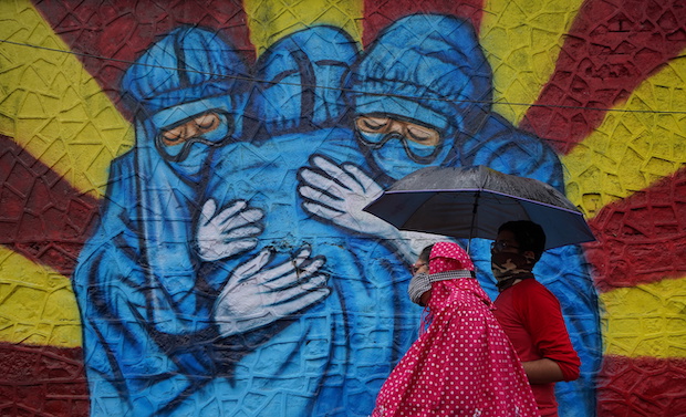 A woman and her son walk past a graffiti on a street, amidst the coronavirus disease (COVID-19) pandemic, in Mumbai