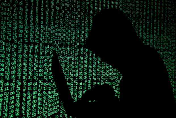 FILE PHOTO: A hooded man holds a laptop computer as cyber code is projected on him in this illustration picture taken on May 13, 2017.  REUTERS/Kacper Pempel/Illustration/File Photo