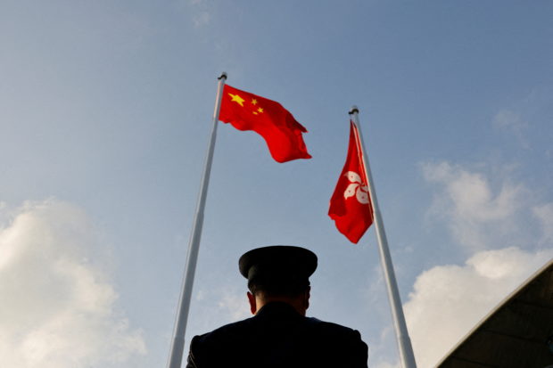 FILE PHOTO: A police officer stands guard below China and Hong Kong flags during a flag raising ceremony, a week ahead of the Legislative Council election in Hong Kong, China, December 12, 2021. REUTERS/Tyrone Siu/File Photo