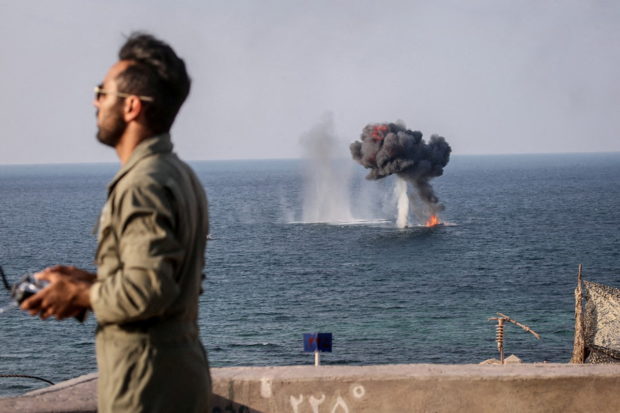 FILE PHOTO: An explosion is seen on the water surface behind a member of the Islamic Revolution Guards Corps (IRGC) during a joint military exercise called the 'Great Prophet 17' in the southwest of Iran, in this picture obtained on December 22, 2021. IRGC/WANA (West Asia News Agency)/Handout via REUTERS