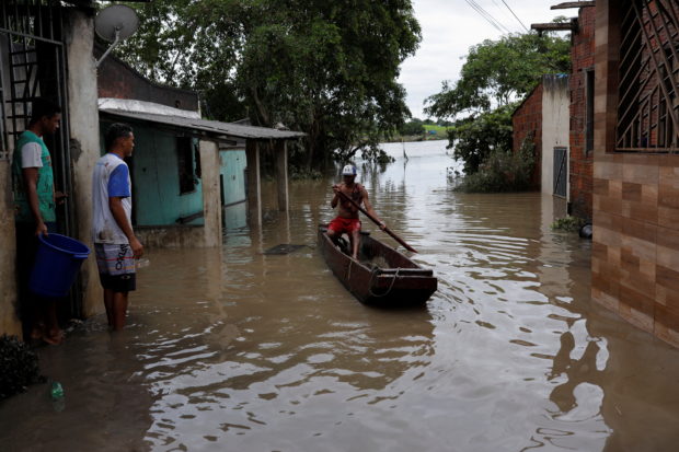 A man paddles a canoe along a street, during floods caused due to heavy rains, in Itabuna, Bahia state, Brazil December 27, 2021. REUTERS/Amanda Perobelli