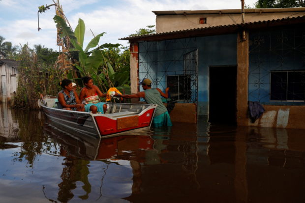Sergio da Silva dos Santos hands clothes to other residents in front of a flooded house accessed by canoe at Sambaituba in Ilheus, Bahia state, Brazil December 29, 2021. REUTERS/Amanda Perobelli/File Photo