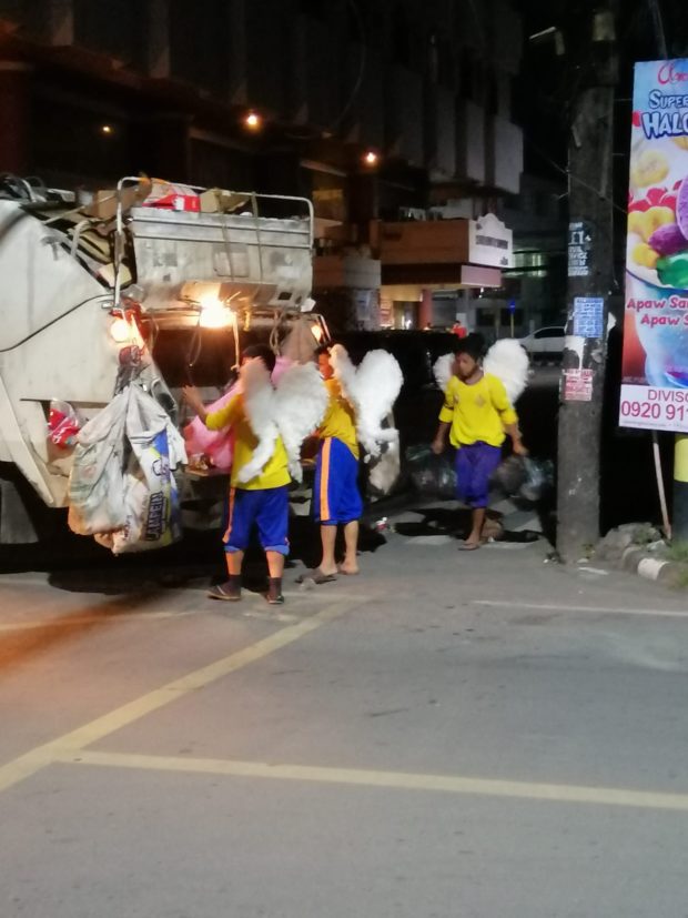 three trash collectors wearing yellow t-shirts, blue shorts, and angel wings