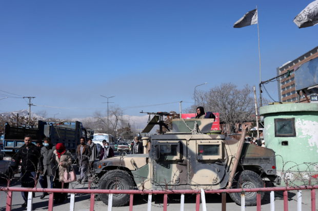 Afghans walk past a Humvee with a Taliban fighter on it guarding the road in Kabul, Afghanistan, January 27, 2022. REUTERS/Ali Khara