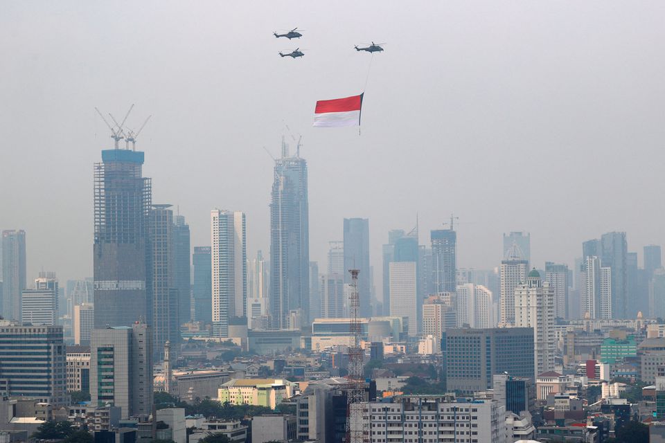 Indonesian Air Force helicopters carrying a big flag fly above high rise buildings