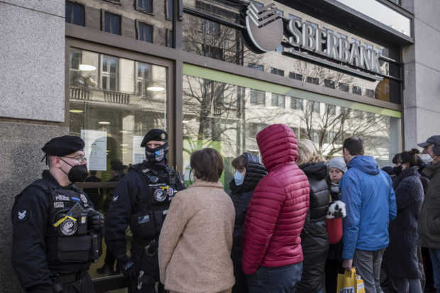 Police guard the bank's entrance as people queue outside a branch of Russian state-owned bank Sberbank to withdraw their savings and close their accounts in Prague on February 25, 2022, before Sberbank will close all its branches in the Czech Republic later in the day. - US President Biden was the first to announce sanctions, hours after Russian President Putin declared a "military operation" into Ukraine. The first tranche will hit four Russian banks -- including the country's two largest, Sberbank and VTB Bank -- cut off more than half of Russia's technology imports, and target several of the country's oligarchs. (Photo by Michal Cizek / AFP)