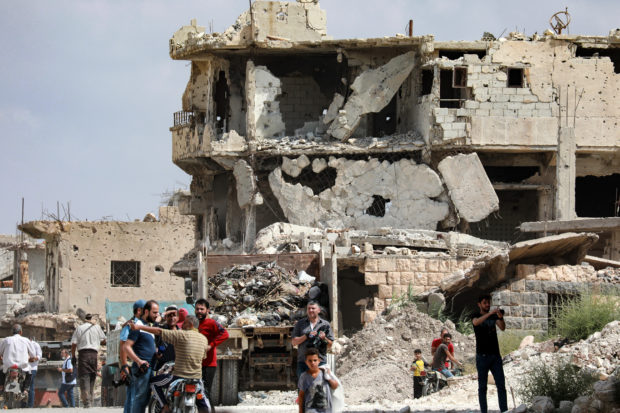  people gathered in front of a heavily damaged building in the district of Daraa al-Balad of Syria's southern city of Daraa, on