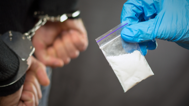 Stock photo of man in handcuffs and gloved hand holding a sachet with powder. STORY:  P8.8-million crystal meth seized from 3 suspects