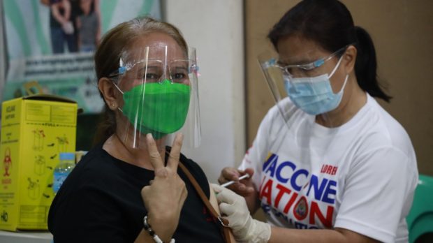 A senior resident of Navotas City receives her COVID-19 booster shot. A health worker conducts a swab test on a woman in Navotas City. Image from Facebook/ Navoteño Ako-Navotas City PIO