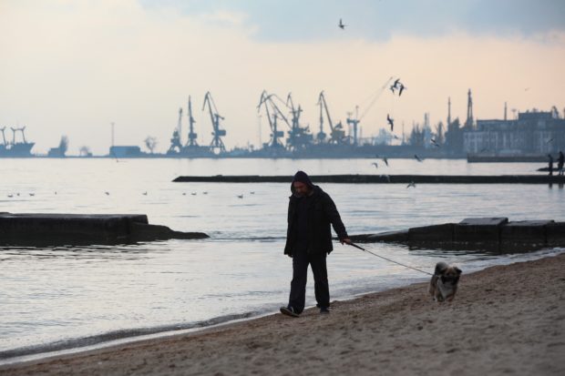 A man walks a dog along a coast of the Sea of Azov in Ukraine's industrial port city of Mariupol on February 23, 2022. - Mariupol lies on the edge of the front line separating government-controlled territory from that overseen by Russian-backed separatists in the rebel stronghold Donetsk. (Photo by Aleksey Filippov / AFP)
