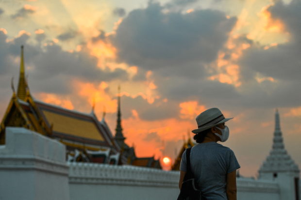 FILE PHOTO: A tourist wears a face mask to prevent spread of the coronavirus disease (COVID-19) during sunset near the Grand Palace in Bangkok, Thailand, January 7, 2022. REUTERS/Chalinee Thirasupa/File Photo
