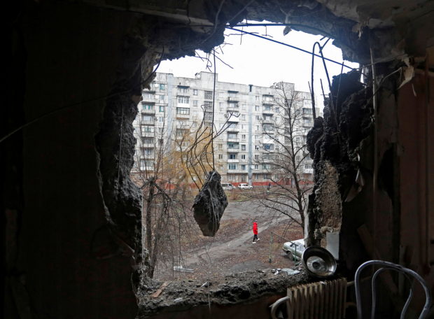 A person walking on the street is pictured through a hole in the wall of a residential building, which locals said was damaged by recent shelling, in the separatist-controlled town of Horlivka (Gorlovka) in the Donetsk region, Ukraine March 2, 2022. REUTERS/Alexander Ermochenko