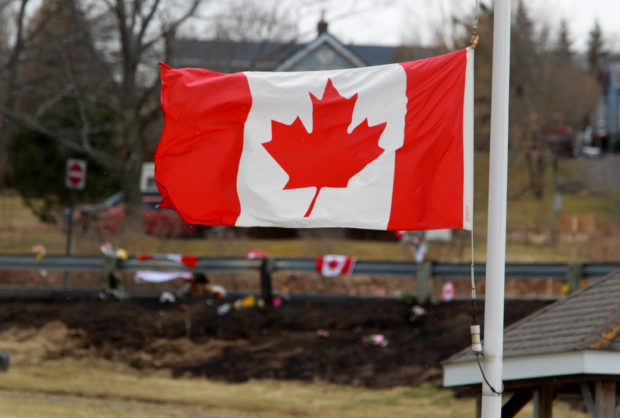 A Canadian flag flies at half-staff backdropped by the makeshift memorial for Royal Canadian Mounted Police (RCMP) Constable Heidi Stevenson, who was shot dead along with multiple others, in Shubenacadie, near Enfield, Nova Scotia, Canada April 22, 2020. REUTERS/Tim Krochak