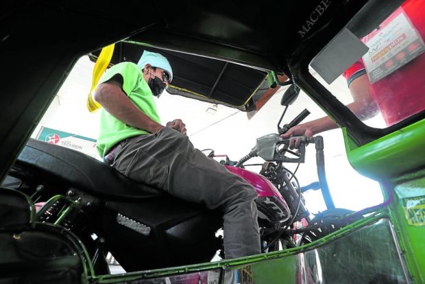 A tricycle driver searches his pocket for bills and coins to pay for fuel at a gasoline station . STORY: Fuel prices roll back – a little