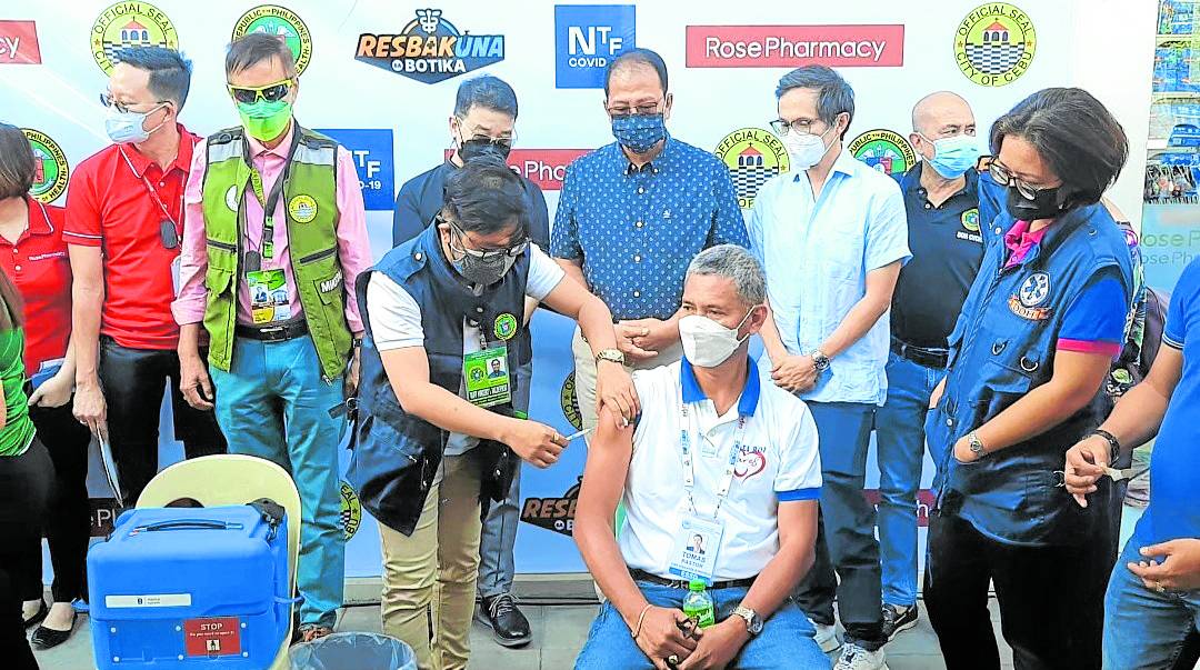 A local health officer vaccinates a man in a pharmacy in Cebu City as officials of the national pandemic task force look on in this February 2022 photo.