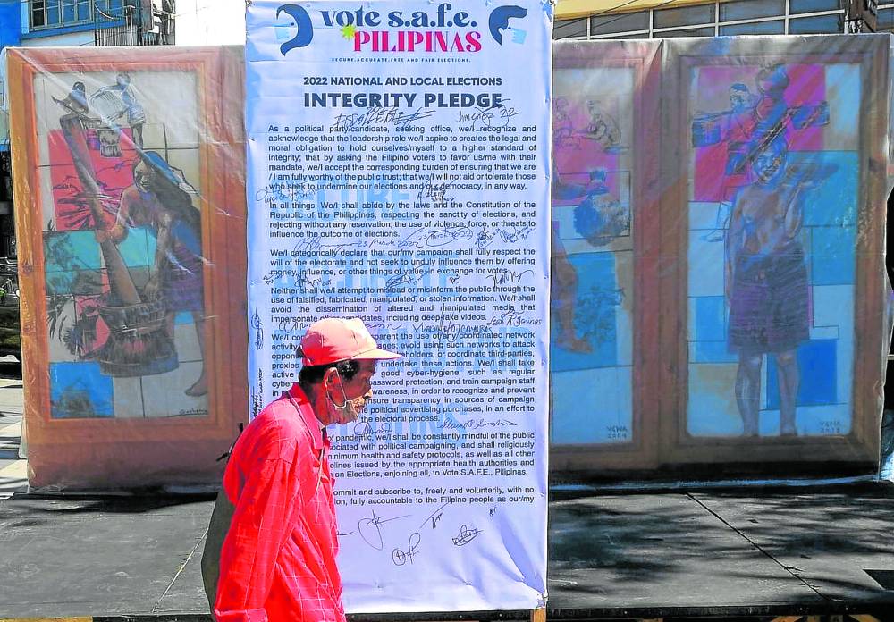 A Baguio resident passes by an integrity covenant signed by candidates in the city after a unity walk for peaceful and honest elections 