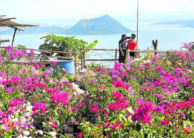 WHILE IT’S SAFE Tourists snap a selfie in Tagaytay City overlooking a seemingly calm Taal Volcano on Sunday, March 27, 2022. STORY: Officials to Taal evacuees: Still risky to go home