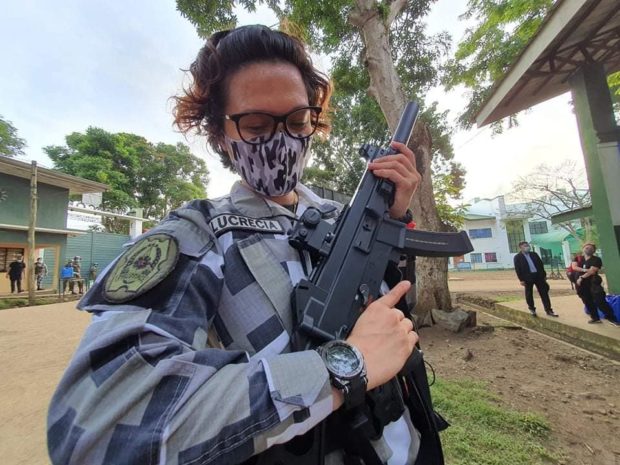 Major Zeerah Blanche Lucrecia in camouflage uniform, holding a gun.
