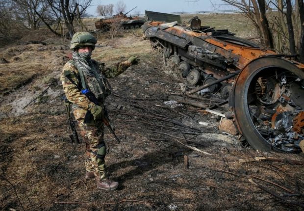 Ukrainian serviceman stands near the wreck of a Russian Armoured Personnel Carrier