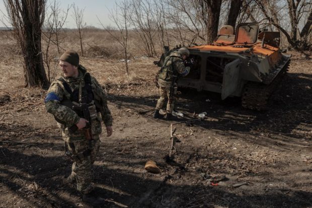 Ukrainian soldiers stand near a wrecked Russian armoured vehicle
