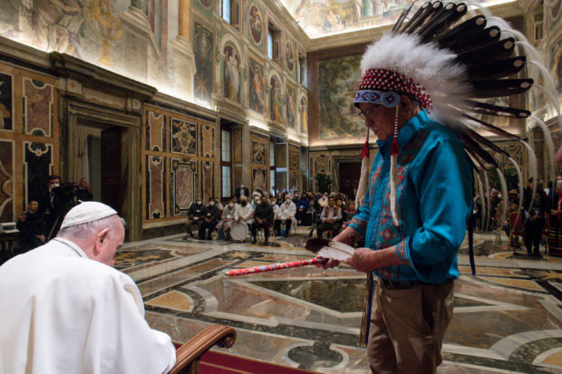 This photo taken and handout on April 01, 2022 shows Pope Francis receiving a gift from a delegation's chief during an audience to Canada's Indigenous delegations at the Vatican. - Pope Francis on April 01 apologised for the decades of abuse at church-run residential schools in Canada and said he would visit the country in late July. (Photo by Handout / VATICAN MEDIA / AFP) / RESTRICTED TO EDITORIAL USE - MANDATORY CREDIT "AFP PHOTO / VATICAN MEDIA" - NO MARKETING - NO ADVERTISING CAMPAIGNS - DISTRIBUTED AS A SERVICE TO CLIENTS