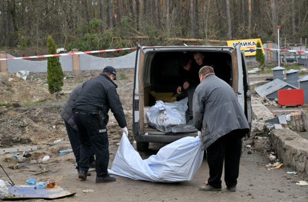 Graphic content / Ukrainian rescuers load the bodies which were discovered in a manhole at a petrol station in the outskirts of the Buzova village, west of Kyiv, on April 10, 2022. - At least two bodies, appearing to be clad in a mix of civilian and military clothing, were discovered in a manhole at the back of a destroyed motorway petrol station. (Photo by Sergei SUPINSKY / AFP)