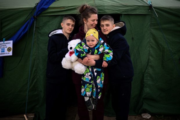 Ukrainian refugee Tetyana Dzymik (C), a 38-year-old drawing teacher from a village near Bucha, poses for a picture along with her children, twins Ivan and Danylo, and baby Oleksiy, as they stand at the entrance to an NGO tent after crossing the Ukrainian-Slovakian border into Slovakia at the Vysne Nemecke border crossing, eastern Slovakia on April 8, 2022. - A heartbreaking human drama is playing out along Ukraine's borders -- fleeing refugees pass the homesick going back, while others who left and then returned flee for their lives for a second time. (Photo by Christophe ARCHAMBAULT / AFP)