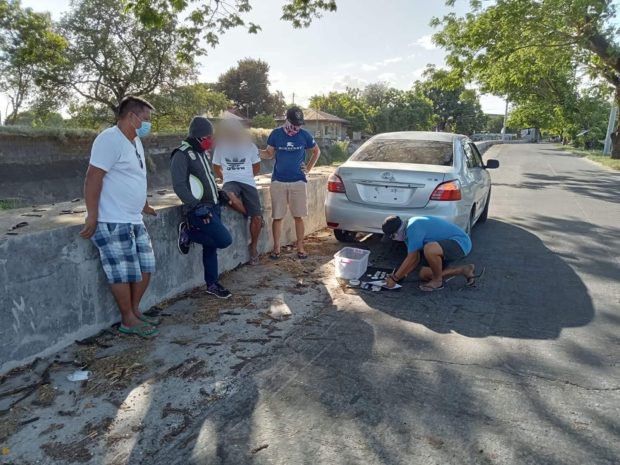 Plainclothes police accost the suspected drug peddler (middle) while inspecting the pieces of evidence allegedly seized Wednesday, March 30, from the latter in Guagua town, Pampanga province. (Photo courtesy of Police Regional Office 3)