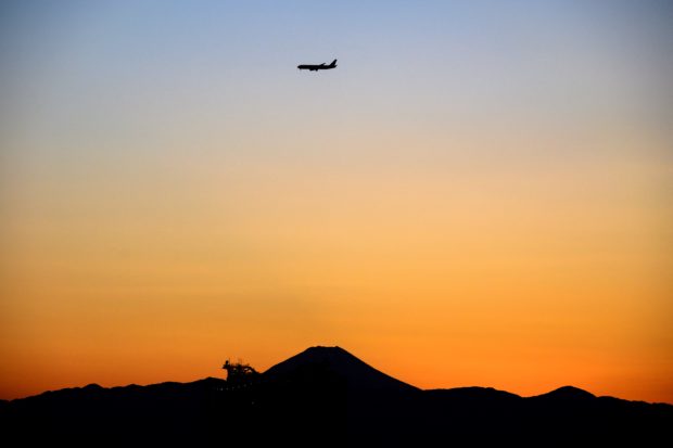 A passenger jet (top) approaches Haneda airport in Tokyo on February 9, 2021, as the silhouette of Mount Fuji (bottom), Japan's highest mountain at 3,776 meters (12,388 feet), is pictured in the distance at sunset. (Photo by Charly TRIBALLEAU / AFP)