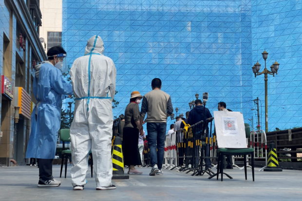 Workers in protective suits stand next to people lining up a makeshift nucleic acid testing site during a mass testing for the coronavirus disease (COVID-19) in Chaoyang district of Beijing, China May 4, 2022. REUTERS/Alessandro Diviggiano