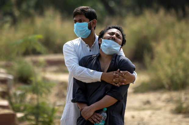 A man is consoled by his relative as he sees the body of his father, who died from the coronavirus disease (COVID-19), before his burial at a graveyard in New Delhi, India, April 16, 2021. REUTERS/Danish Siddiqui