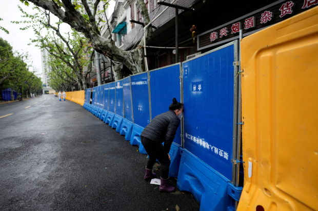 A woman tries to buy food from a vendor behind barricades of a sealed-off area, during lockdown amid the coronavirus disease (COVID-19) pandemic, in Shanghai, China April 14, 2022. REUTERS/Aly Song/File Photo