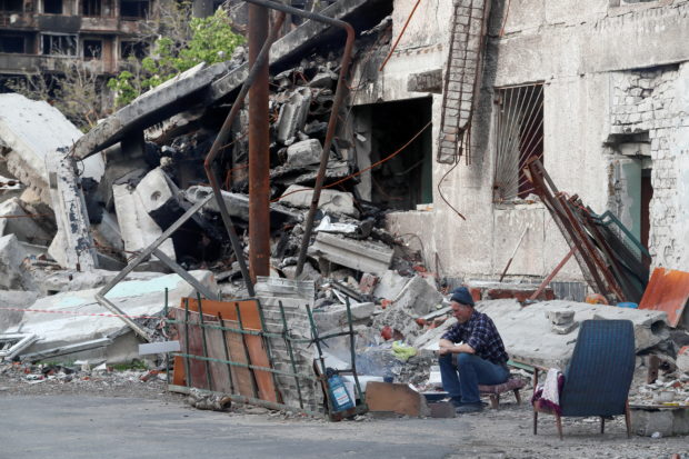 A local resident sits in a courtyard outside a building heavily damaged during Ukraine-Russia conflict in the southern port city of Mariupol, Ukraine May 15, 2022. REUTERS/Alexander Ermochenko