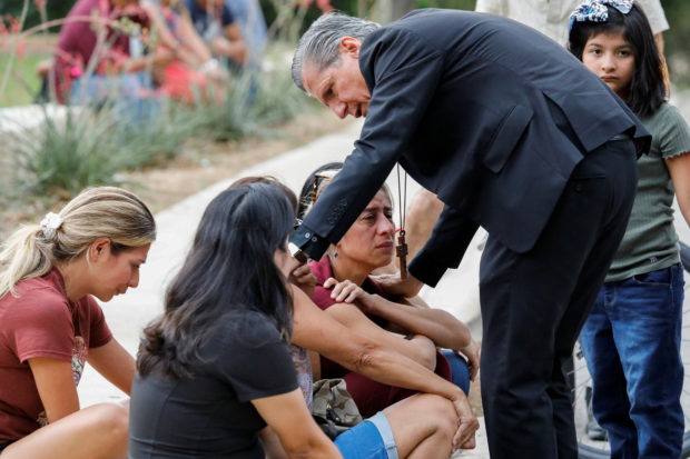 A priest comforts people as they react outside the Ssgt Willie de Leon Civic Center, where students had been transported from Robb Elementary School after a shooting, in Uvalde, Texas, U.S. May 24, 2022. REUTERS/Marco Bello