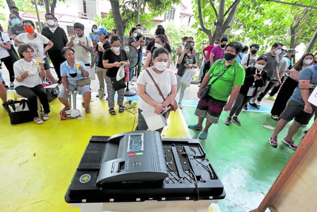 Voters are forced to wait in line after the vote-counting machine (VCM) at their assigned precinct malfunctioned in North Susana Executive Village, Quezon City, on Monday. STORY: VCM glitches bug polls; Comelec finally not reusing them in 2025
