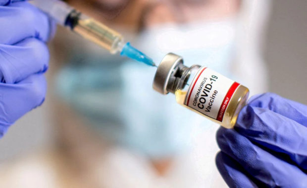 A woman holds a small bottle labelled with a "Coronavirus COVID-19 Vaccine" sticker and a medical syringe. STOROY: Senate inquiry into wasted vaccines set