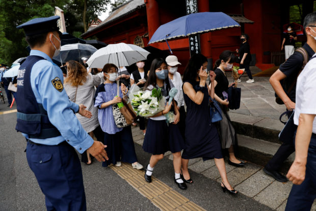 A police officer stands guard as people line up to offer flowers at Zojoji Temple, where the funeral of the late former Japanese Prime Minister Shinzo Abe, who was shot while campaigning for a parliamentary election, will be held in Tokyo, Japan July 12, 2022. REUTERS/Issei Kato