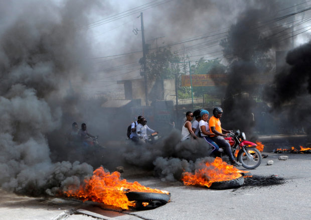 FILE PHOTO: Motorcycle drivers pass through a burning road block as anger mounted over fuel shortages that have intensified as a result of gang violence, in Port-au-Prince, Haiti, July 13, 2022. REUTERS/Ralph Tedy Erol/File Photo