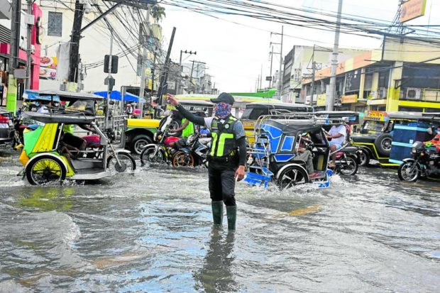 GO WITH THE FLOW A traffic enforcer ensures that vehicles flow smoothly at Dagupan City’s commercial district despite the high tide on Thursday. Many Dagupeños have learned to live with floods and the rising tide as the city faces Lingayen Gulf and is crisscrossed by seven rivers. —WILLIE LOMIBAO