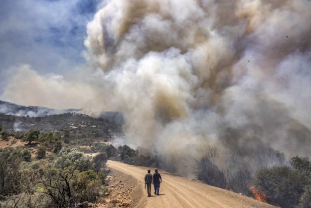 Men walk along a dirt road as a wild forest fire rages near the Moroccan city of Ksar el-Kebir in the Larache region on July 14, 2022. 