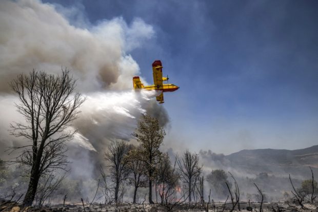 A Royal Moroccan Air Force Canadair CL-415 firefighting aircraft douses a wildfire with retardant spray to extinguish a wild forest fire raging near the Moroccan city of Ksar el-Kebir in the Larache region on July 14, 2022.